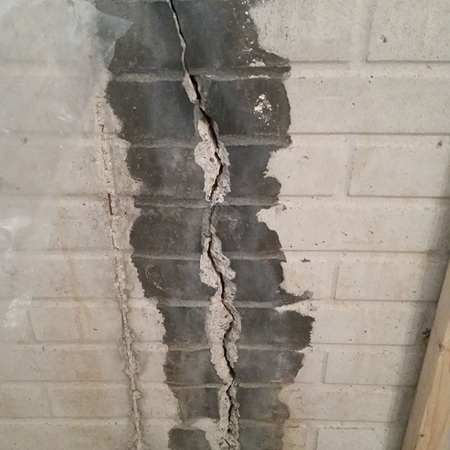 Before - A basement wall with a large crack before repair.